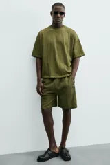 Bermuda de algodón color verde oliva, con corte relajado y textura acanalada vertical. Presenta cintura elástica con cordón interior y bolsillos laterales y trasero.