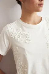 Remera de manga corta color crudo con apliques florales bordados tono sobre tono en el frente.