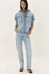 Cazadora de denim oversize con capucha gris desmontable, cuello camisero, cierre frontal con botones metálicos y bolsillos delanteros de plastrón.