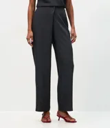 Pantalón de sastrería color gris oscuro, de tiro alto y corte recto. Presenta un diseño sofisticado con un cruce frontal superpuesto en la cintura y cierre oculto.