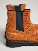 Bota tipo chelsea de cuero con textura de reptil, color suela. Presenta paneles elásticos laterales en color negro, suela de goma dentada con pespuntes en contraste y puntera redondeada.