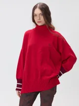 Pullover de punto color rojo, con cuello tortuga, corte holgado y mangas largas con puños acanalados en contraste con rayas blancas. Presenta un logo bordado en el pecho.