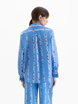 Camisa de calce holgado color azul, confeccionada en poplin satinado con estampado de motivos florales verticales. Presenta cuello clásico, mangas largas con puños abotonados y cierre frontal con botones.