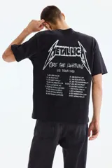 Remera negra de corte holgado con hombros caídos y cuello redondo. Presenta un estampado frontal pequeño con el logo de Metallica y la inscripción 'U.S. Tour 1985'.