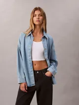 Camisa de denim de corte holgado, con cuello en punta, mangas largas y cierre frontal con botones. Presenta un diseño clásico con acabado lavado y monograma bordado en el pecho.