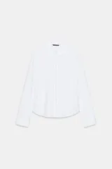 Camisa de popelín color blanco con cuello solapa redondeado y manga larga. Presenta un cierre frontal con botones ocultos y una tapeta decorada con perlas.