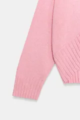 Sweater de punto color rosado con cuello redondo y manga larga, de bajo asimétrico con acabados en rib.