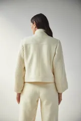 Campera de lana fina color crema, con cuerpo estructurado y mangas de tejido de punto acanalado. Presenta cuello alto, cierre frontal con botones y bolsillos laterales con doble abertura.