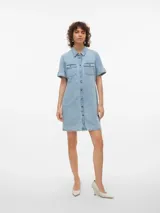 Vestido corto de denim en tono celeste claro, con cuello camisero, cierre frontal con botones metálicos, bolsillos con solapa en el pecho y mangas cortas con vuelta.