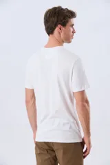 Remera blanca de manga corta y cuello redondo, con estampa frontal inspirada en el mar y atardeceres de verano con la inscripción 'Travel. Beach. Repeat.' y 'Legacy'.
