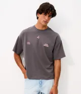 Remera gris oscuro de corte oversized con cuello redondo y manga corta. Cuenta con estampa frontal en color rosado con texto "LEAD THE WAY", tres estrellas y grafismo de números.