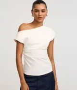 Blusa blanca de corte ajustado, con diseño asimétrico de un solo hombro, manga corta estructurada y detalle drapeado en el lateral de la cintura.