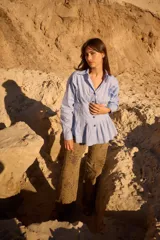 Camisa de silueta entallada con diseño tipo corset, destacada por alforzas verticales en la cintura que aportan estructura. Presenta cuello clásico, cierre frontal con botones y mangas largas con puños abotonados.