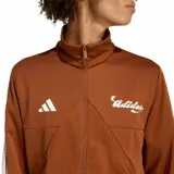 Campera deportiva Adidas House of Tiro color marrón, con cierre frontal completo, cuello alto, bolsillos laterales y las icónicas tres rayas blancas en las mangas. Presenta el logo de la marca y un diseño gráfico en el pecho.