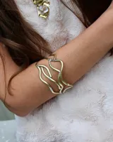 Brazalete rígido dorado con diseño abstracto de líneas onduladas.