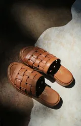 Sandalias planas de cuero con tiras plateadas tejidas en el empeine y base marrón.
