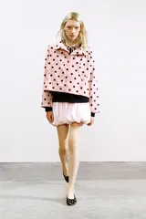 Chaqueta de cuello subido ajustable con lazada, manga larga y cierre frontal con botones. Presenta un diseño estampado de lunares negros sobre fondo rosado, bolsillos laterales y bajo ajustable con cordones.