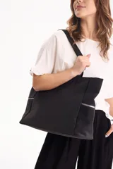 Cartera tipo shopper color negro, confeccionada en poliuretano, con bolsillos laterales con cierre y correa larga ajustable.