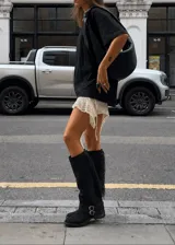 Bota alta de gamuza negra con caña alta, flecos laterales, tiras con hebillas metálicas en el tobillo y taco cuadrado.