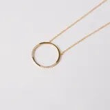 Collar de cadena fina con dije circular, elaborado en plata 925 con baño de oro. El dije presenta un diseño minimalista con incrustaciones de circonias en dos secciones opuestas del círculo.
