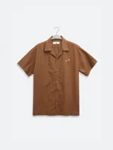 Camisa azul de hombre de calce relajado y corte cuadrado, confeccionada en una mezcla liviana de lino y algodón. Presenta cuello tipo camp, cierre con botones de madera grabados con el logo y un bordado sutil en el pecho izquierdo con forma de palmera. Incluye patch con logo de la marca.