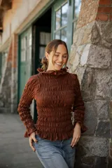 Blusa de muselina de algodón color beige, con diseño totalmente fruncido, cuello alto, mangas largas y terminaciones con volados en cuello, puños y ruedo.