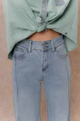 Pantalón de jean color arena con silueta wide leg, tiro medio-alto y costuras verticales delanteras que estilizan la figura. Cuenta con bolsillos funcionales y cierre frontal con doble botón.