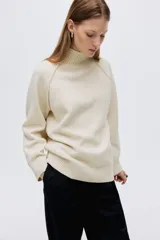 Buzo de punto oversized con cuello tortuga acanalado y abertura en la nuca. Presenta mangas raglán con costuras decorativas y terminaciones acanaladas en puños y bajo.
