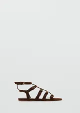 Sandalias planas de gamuza marrón con diseño de múltiples tiras cruzadas y hebillas metálicas doradas. Cuenta con cierre de hebilla en el tobillo.
