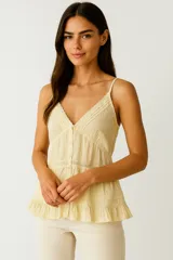 Musculosa de algodón con breteles finos tipo lencero, escote en V profundo con detalle de encaje, cierre frontal con botones y diseño con volados en el ruedo.