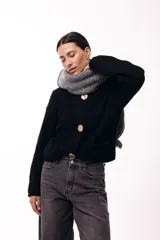 Saco de tejido de punto grueso en color negro, con cuello redondo y cierre frontal mediante tres botones metálicos grandes de acabado texturizado. Presenta bolsillos delanteros y mangas largas con puños ajustados.