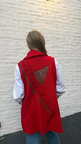 Chaleco largo de lana color rojo con cuello tipo chal acanalado. Presenta cierre frontal mediante tres trabas de cuero con botones tipo cuerno y bolsillos frontales con detalles en cuero.