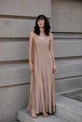Vestido largo de seda color beige, con breteles finos ajustables, escote en V y diseño fluido con volado en la parte posterior.