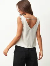 Blusa sin mangas color blanco off-white, con escote en V y detalles de encaje en los tirantes. Diseño holgado y fluido.