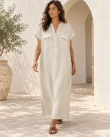 Vestido camisero largo de lino color blanco, con cuello en V, mangas cortas con vuelta y bolsillos frontales con solapa. Cuenta con cierre de botones en la parte superior.