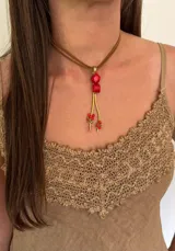 Collar corto con doble cordón marrón y dije colgante con cuentas rojas y detalles dorados.