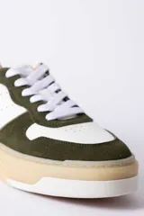 Championes urbanos Urban Haus modelo Mauro, con diseño de paneles en cuero blanco y gamuza verde oliva. Presentan suela de plataforma de goma en tono beige, cierre con cordones blancos y logo de la marca grabado en el lateral.
