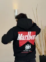 Canguro negro con capucha, de corte boxy, con estampa gráfica en la espalda que recrea el logo de Marlboro en rojo y blanco, junto con el escudo de Philip Morris y la leyenda 'Smoking kills' y 'FILTER BLACK'.