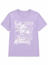 Remera blanca con estampado frontal de la leyenda "OUT OF OFFICE", un sol amarillo y ondas rosadas, acompañada por el texto "slow living by the sea".