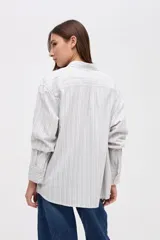 Camisa de corte oversize con diseño de rayas verticales finas en tonos claros. Presenta cuello clásico, cierre frontal con botones y mangas largas con puños abotonados.