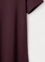 Camiseta deportiva de manga corta en color bordó, con diseño de cuello redondo y paneles laterales con perforaciones para mayor ventilación. Presenta un pequeño logo reflectante en la parte inferior.