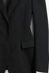 Blazer negro de corte recto de la colección Zara Studio, con solapas de muesca, cierre frontal de dos botones y bolsillos con solapa. Presenta mangas largas con pliegues estructurados en los hombros y forro interior a rayas a contraste.