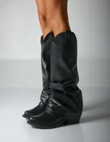 Bota de caña alta color negro, de cuero sintético, con punta cuadrada y efecto arrugado en el tobillo.