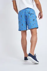 Short de baño con cintura elástica y cordón ajustable, confeccionado en tela ligera de secado rápido. Presenta un estampado botánico integral en tonos amarillos, blancos y azules, con dos bolsillos delanteros y uno posterior.