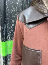 Camisa de tejido de punto color marrón con cuello, bolsillos frontales, puños y hombros de cuero sintético en color marrón oscuro, y cierre frontal con botones.