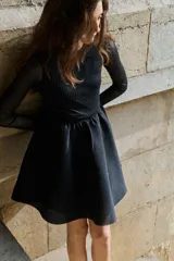 Vestido corto de malla transparente con detalles de strass tono sobre tono. Presenta mangas largas, cuerpo ajustado, escote redondo y cierre oculto en la espalda. Incluye costura fruncida en la cintura y falda con vuelo, con forro parcial.