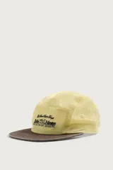 Gorra de 5 paneles de color amarillo claro con tejido ripstop, visera plana marrón de efecto desgastado y bordado frontal en negro. Cuenta con ajuste en la parte posterior.