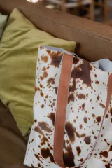 Bolso tipo tote de cuero con pelo color marrón y blanco, con manijas de cuero crudo.