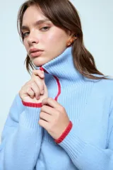 Sweater de punto color celeste con cuello polo y cierre frontal parcial. Presenta detalles de terminación en color rojo en el cuello, puños y ruedo.