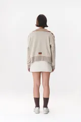 Buzo de tejido de punto en color azul marino, con cuello alto y cierre frontal parcial. Presenta un diseño con franjas en color marrón y detalles de líneas en rojo en el pecho, hombros y ruedo. Tiene corte holgado y mangas largas con puños acanalados.